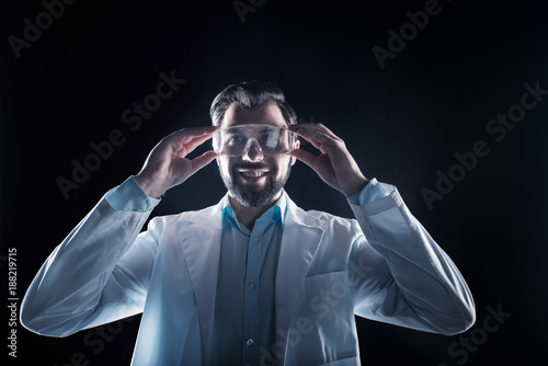 Professional science. Joyful nice happy man smiling and wearing safety glasses while working as a scientist