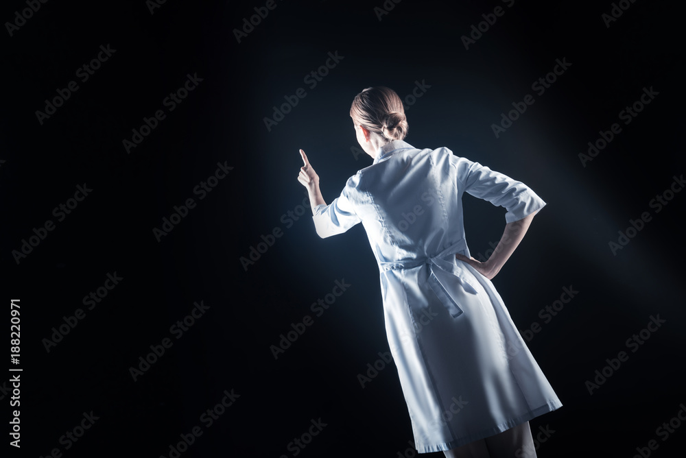 Professional lab. Serious smart female scientist turning her back to you and holding her hand up while working with modern technology Professional lab. Serious smart female scientist turning her back to you and holding her hand up while working with modern technology