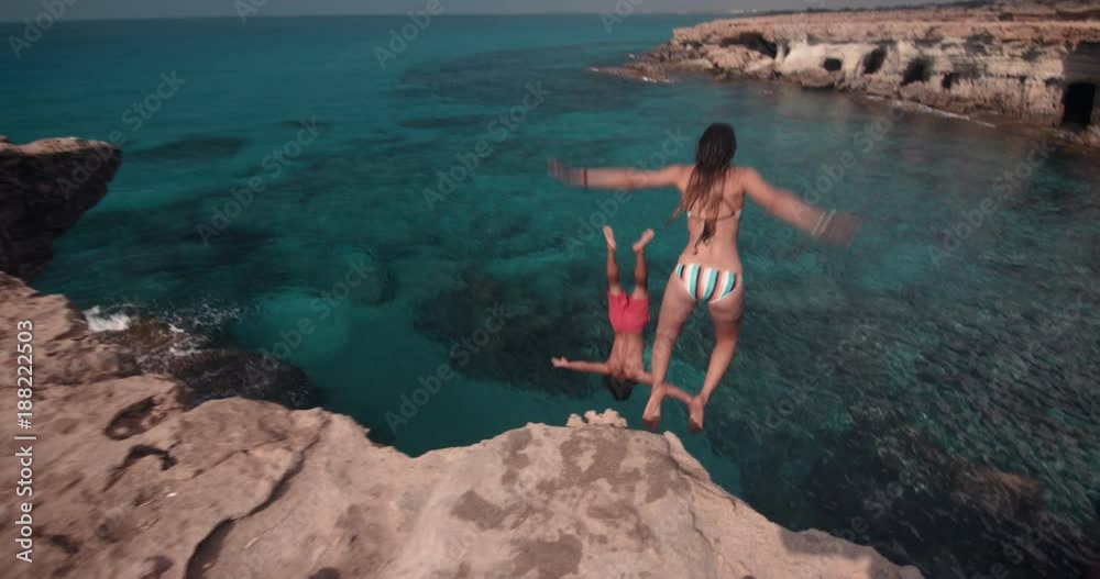 Young active couple jumping off cliff and diving into ocean
