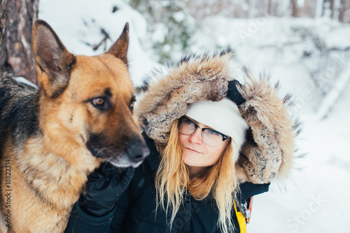 Best friends, young blond woman in winter jacket and hat, stands next to her pet friend a big german shepherd dog. Animal protection day and love for animals