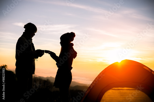 Silhouette couple traveler drinking coffee in the morning with camping tents on the hills under
