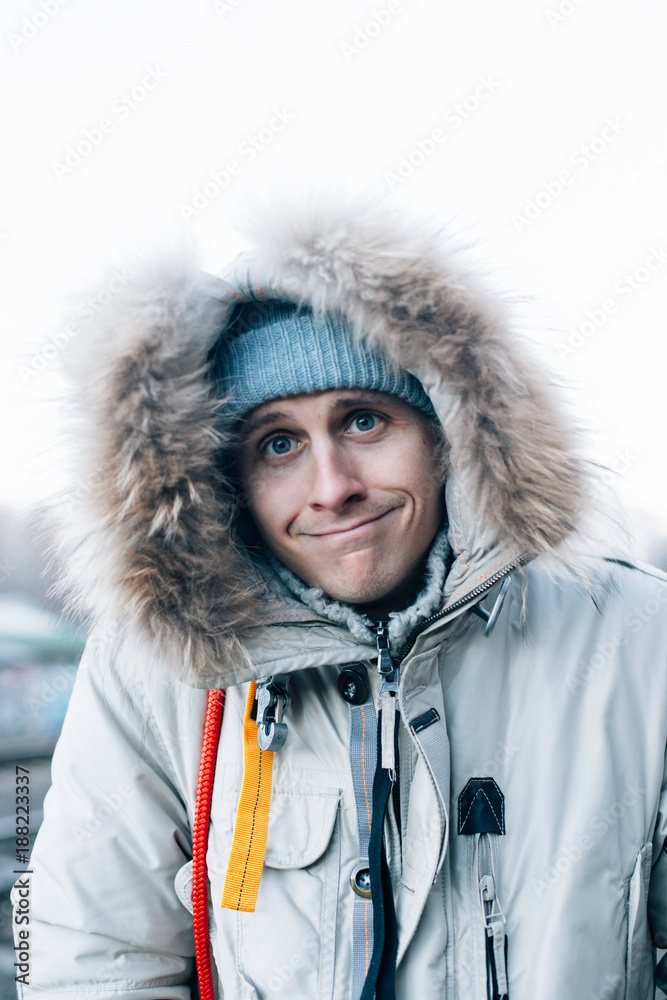 Cute and funny looking young man in huge furry hood from winter jacket  makes silly face