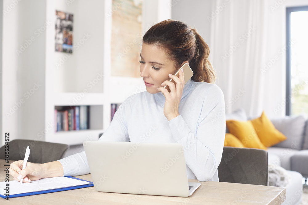 Managing my business from home. A beautiful middle aged woman using laptop and mobile phone while sitting at desk and working from home. Home office. Managing my business from home. A beautiful middle aged woman using laptop and mobile phone while sitting at desk and working from home. Home office.