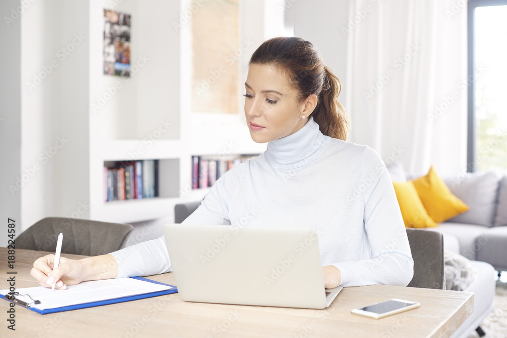 Managing my business from home. A beautiful middle aged woman using laptop and mobile phone while sitting at desk and working from home. Home office. Managing my business from home. A beautiful middle aged woman using laptop and mobile phone while sitting at desk and working from home. Home office.