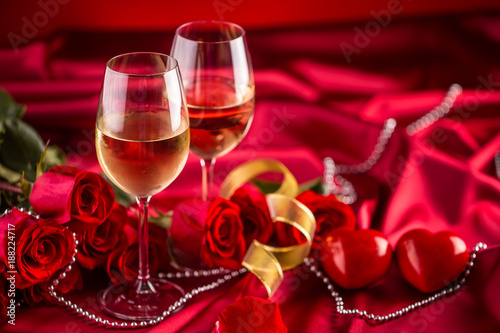 Valentines or wedding concept. Wine cups red roses and romantic setting for t...