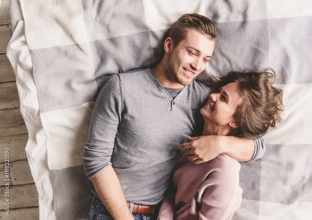 Pretty loving couple is luxuriating in bed together. They are hugging and smiling