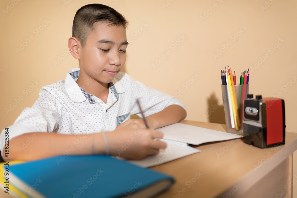 A Little Asian boy use pencil writing on notebook homework