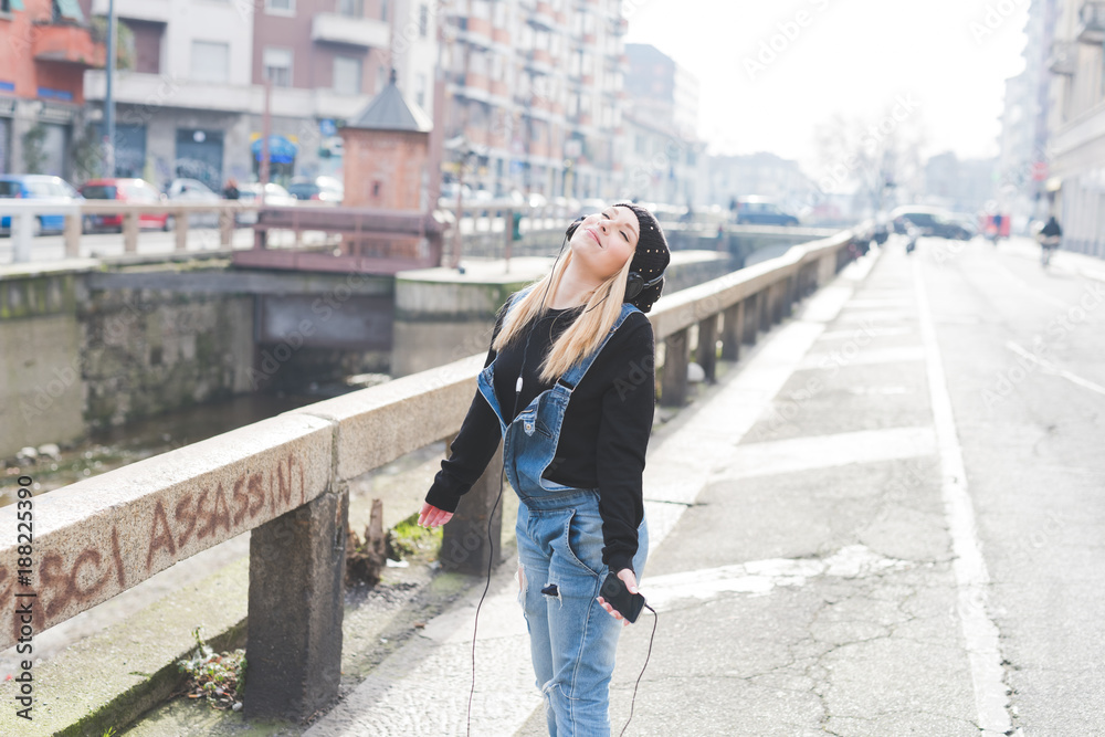 young woman beautiful blonde hair outdoor walking listening music with smart phone hand hold - music, relaxing, technology concept