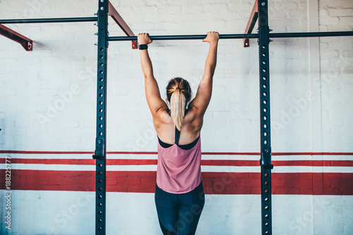 Strong female athlete doing pull up in gym