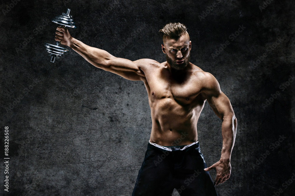 Young male bodybuilder doing exercise with heavy weight dumbbells. Photo of muscular man on dark background. Strength and motivation.