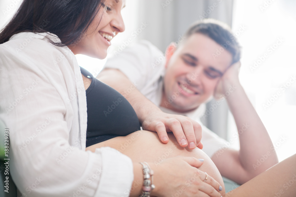 Young pregnant couple relaxing on sofa at home, touching belly Young pregnant couple relaxing on sofa at home, touching belly