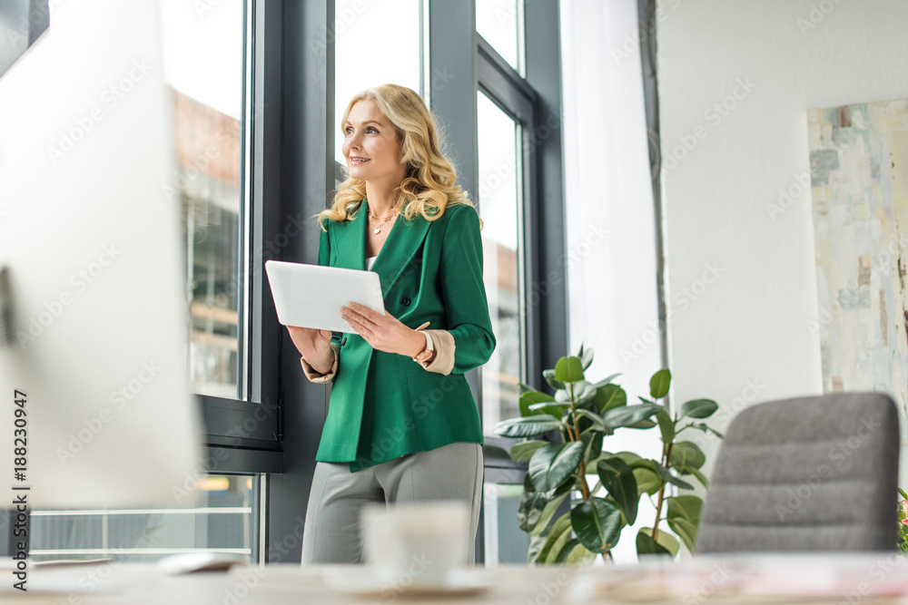 selective focus of smiling middle aged businesswoman holding digital tablet and looking away at workplace selective focus of smiling middle aged businesswoman holding digital tablet and looking away at workplace