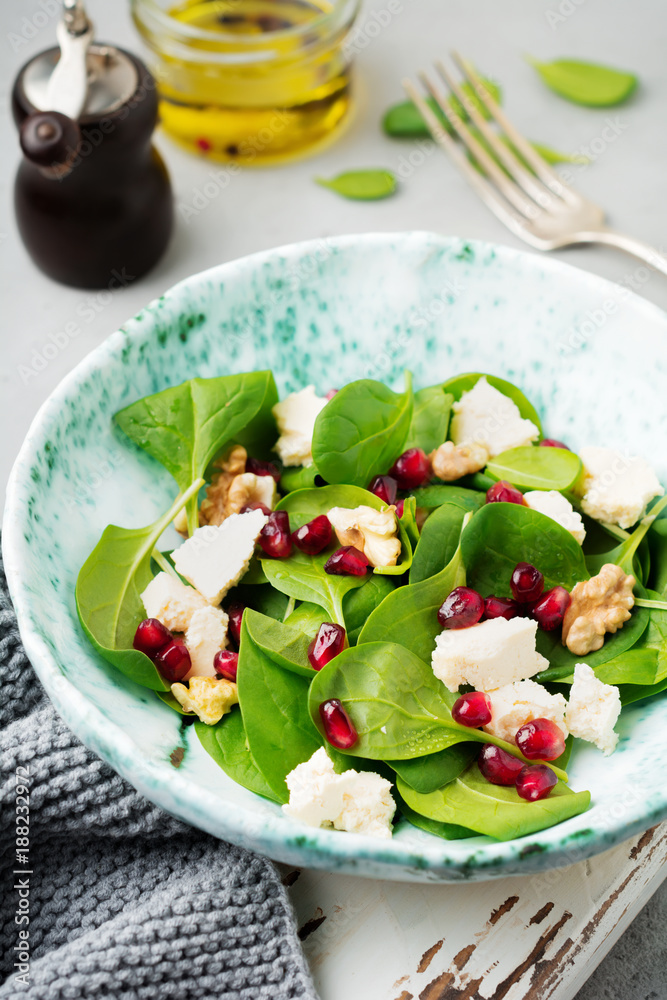 Fresh useful vegetarian wholesome spinach, pomegranate seeds, walnut, saffron, pepper and ricotta salad on gray background. Selective focus. Top view. Copy space for text. Fresh useful vegetarian wholesome spinach, pomegranate seeds, walnut, saffron, pepper and ricotta salad on gray background. Selective focus. Top view. Copy space for text.