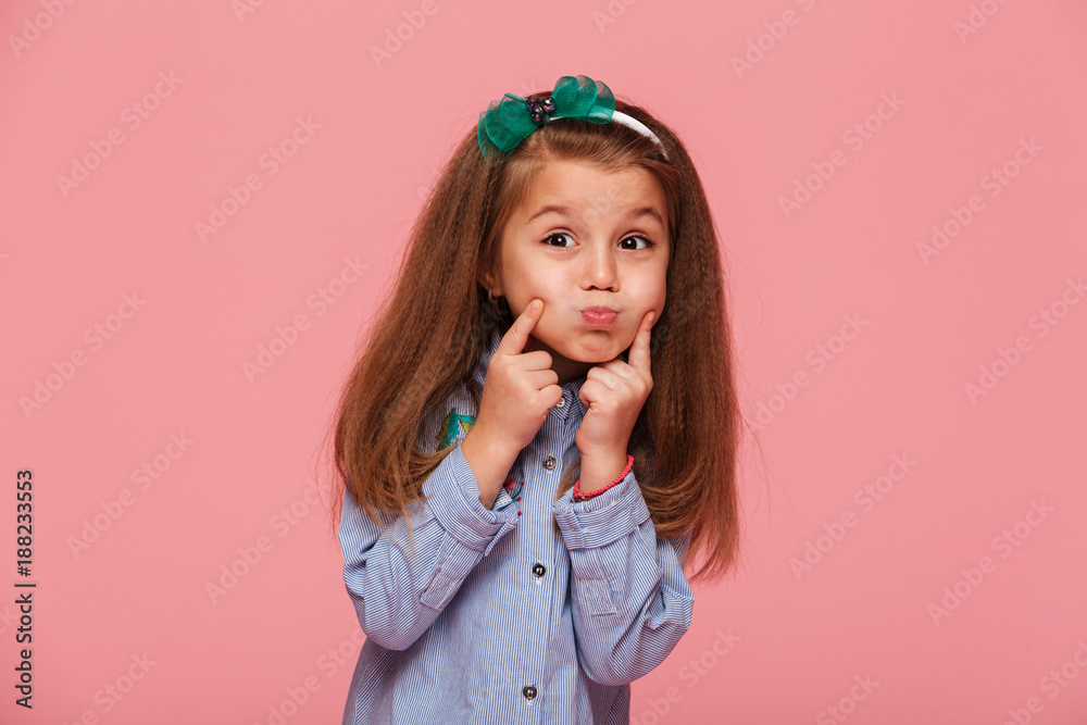 Portrait of adorable little girl 5-6 years with beautiful long auburn hair blowing up her cheeks touching face over pink background - obrazy, fototapety, plakaty 