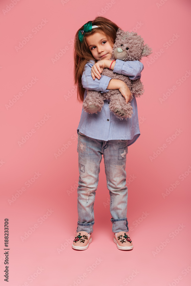 Full-length photo of adorable child girl with long auburn hair and casual clothes hugging her lovely teddy bear isolated over pink background Full-length photo of adorable child girl with long auburn hair and casual clothes hugging her lovely teddy bear isolated over pink background