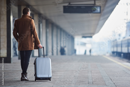 Full length man keeping suitcase while turning back to camera railway station. Trip concept. Copy space © Yakobchuk Olena