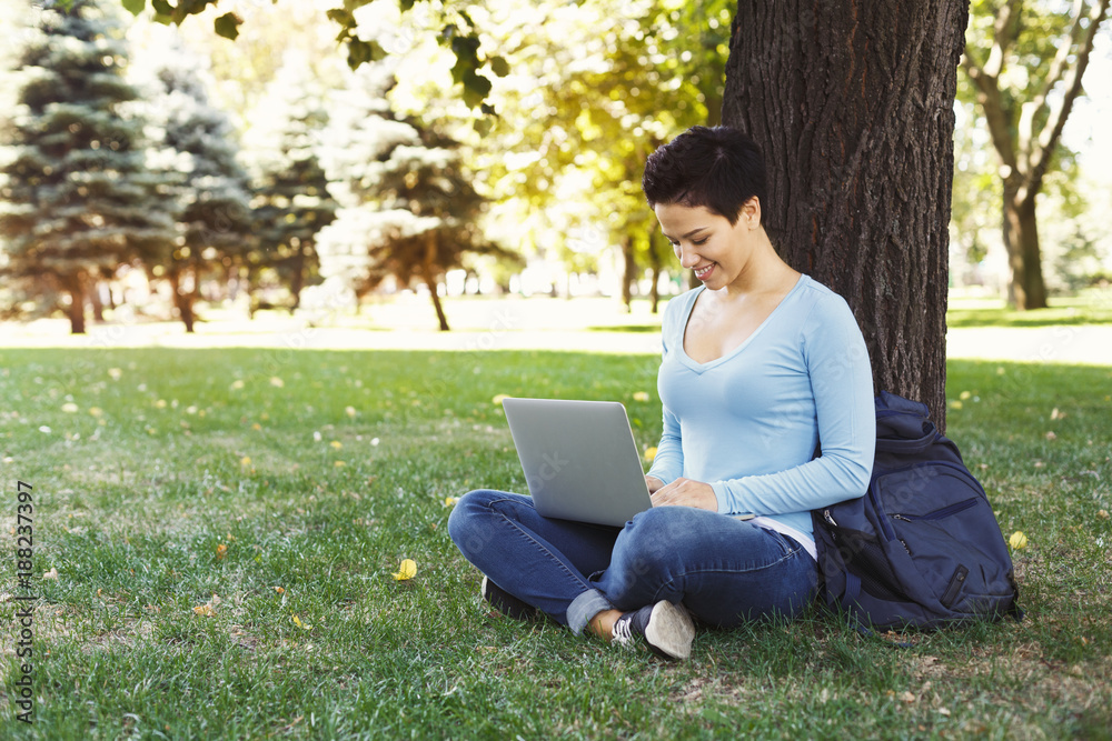 Woman sitting on the grass with laptop outdoors Woman sitting on the grass with laptop outdoors