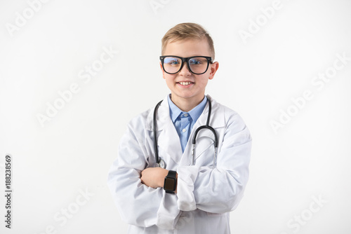 My biggest dream. Portrait of pleased schoolchild seeing himself as an employee in the medical field. Stethoscope is hanging on his neck. Isolated on background