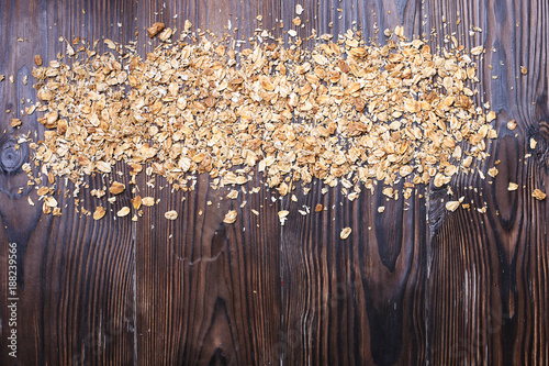 Overhead of granola scattered rolled oats on dark wooden texture table. Healthy nutritious vegan flakes full of carbohydrates and protein for sporty lifestyle. Top view, copy space, background. photo
