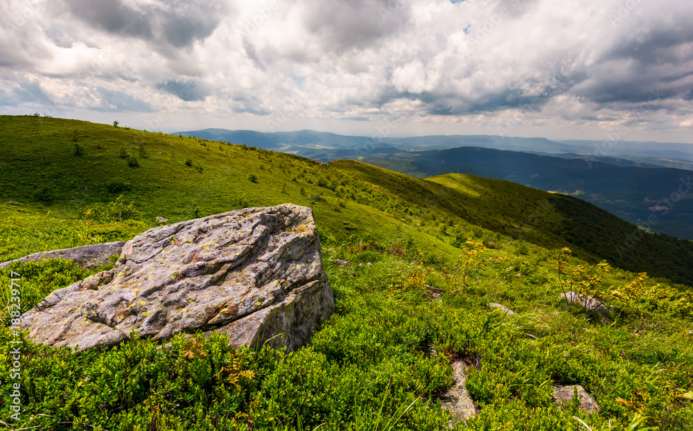 grassy slopes of Carpathian mountains. huge boulder on the edge of a hill side. mountain ridge under the cloudy sky in summer time