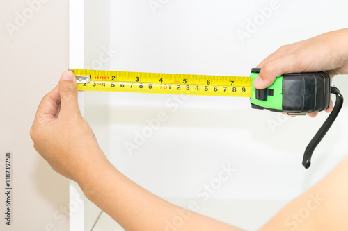 Close up of handyman hands using tape ruler with white cabinet