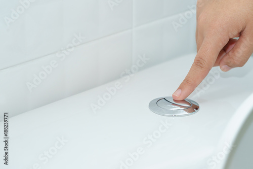 Close up of finger pushing a flush toilet button for cleaning. - save water concept. photo