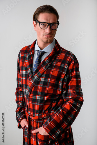 Waist up portrait of assured guy standing with his hands tucked in robe pockets. Isolated on grey background