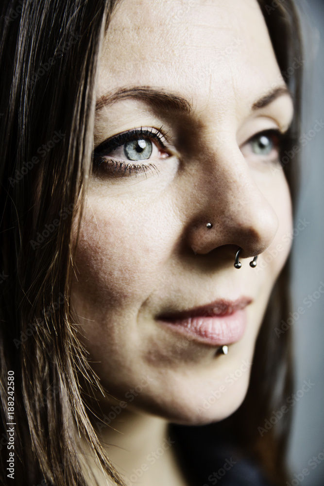 junge Frau mit langem Haar und Piercings im Gesicht, Portrait vor grauem Hintergrund StockFoto