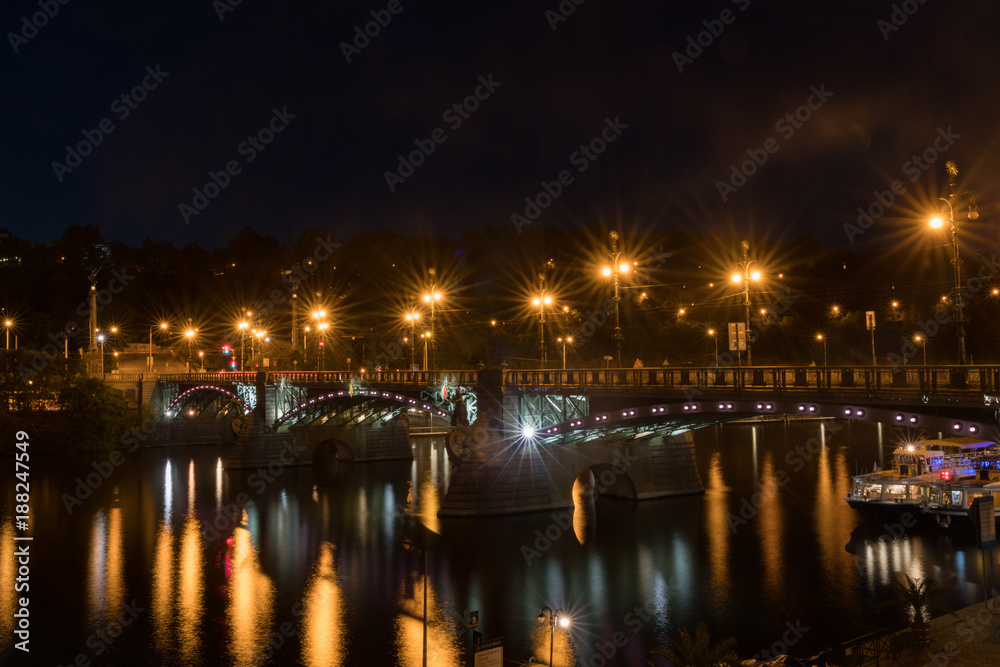 Illuminated bridge across Vltava River with reflections in calm water
