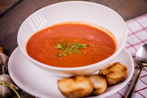 tomato soup with pasta and chives and bread crouton in white plate on wood table 