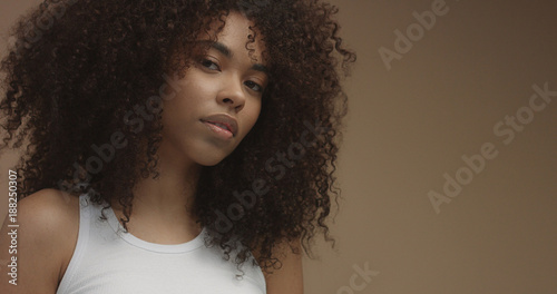 mixed race black woman portrait with big afro hair, curly hair in beige background