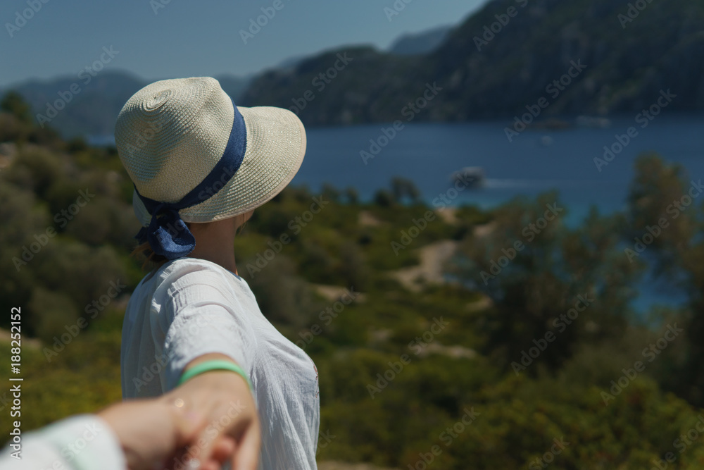 Obraz premium Young girl in hat holding an unknown man's hand and calling after him to enjoy the beautiful nature and the sea while on sunny summer day