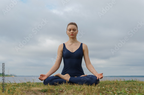 Young attractive girl practicing yoga, sitting in Half Lotus exercise, Ardha Padmasana pose. © lenblr