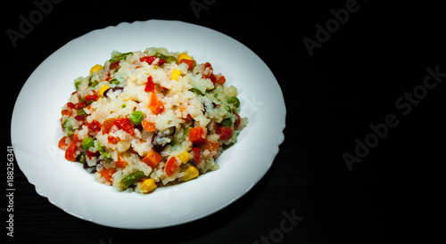 Rice with mixed vegetables on white plate on dark wooden background with copy space.