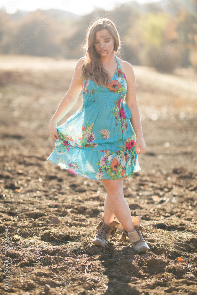 Happy young mixed race woman in blue dress poses in field destroyed by wildfire while covered in ashes Happy young mixed race woman in blue dress poses in field destroyed by wildfire while covered in ashes