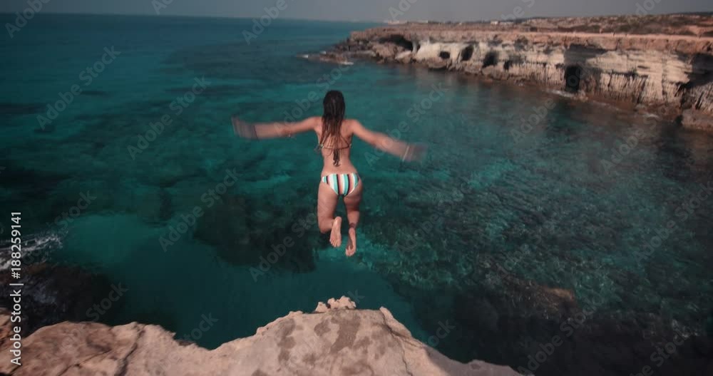 Young woman jumping into ocean from rock cliff