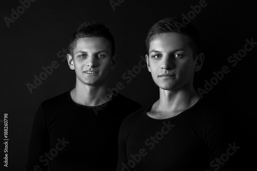 Two attractive positive young twin brothers standing dressed in 