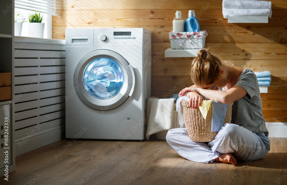 tired housewife woman in stress sleeps in laundry room with washing machine . tired housewife woman in stress sleeps in laundry room with washing machine .