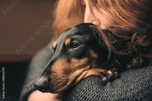 Portrait of a red-haired woman who hugs a sleepy black dog, duchshund.