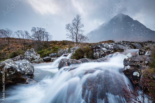 landscape view of scotland and buchaille etive mor with a flowing waterfall and river in the foreground in winter in the highlands of scotland