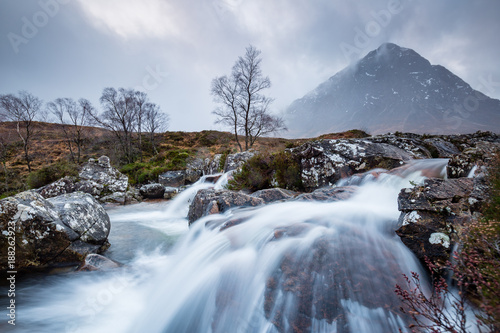 landscape view of scotland and buchaille etive mor with a flowing waterfall and river in the foreground in winter in the highlands of scotland
