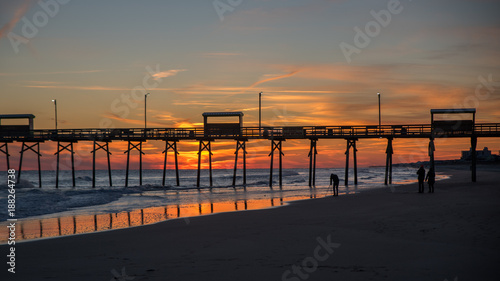 Colorful Sunset at ocean coast with silhouette of pier and photographer