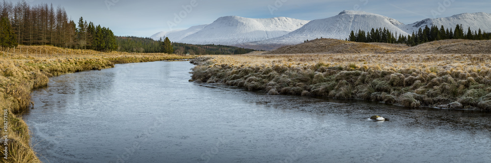 landscape view of scotland and a remote river in the higlands of scotland in panoramic landscape format with snow on the mountain peaks