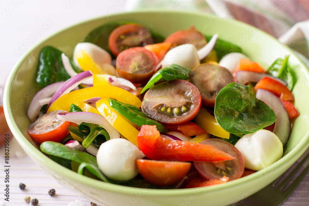 Fresh salad with spinach, bell peppers, tomatoes, red onions and mozzarella on purple wooden background.