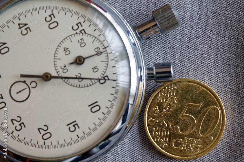 Euro coin with a denomination of 50 euro cents and stopwatch on gray denim backdrop - business background