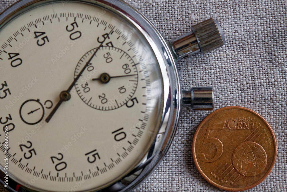 Euro coin with a denomination of 5 euro cents and stopwatch on white linen backdrop - business background
