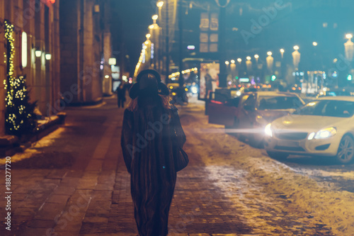 a woman walks down the street at night in the winter