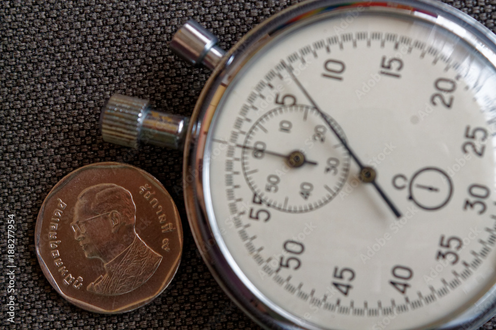 Thai coin with a denomination of five baht (back side) and stopwatch on worn brown jeans backdrop - business background Thai coin with a denomination of five baht (back side) and stopwatch on worn brown jeans backdrop - business background