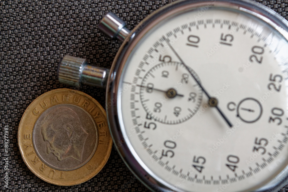 Turkish coin with a denomination of one lira (back side) and stopwatch on brown jeans backdrop - business background