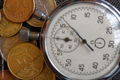 Pile of euro coins with old vintage stopwatch on brown jeans background